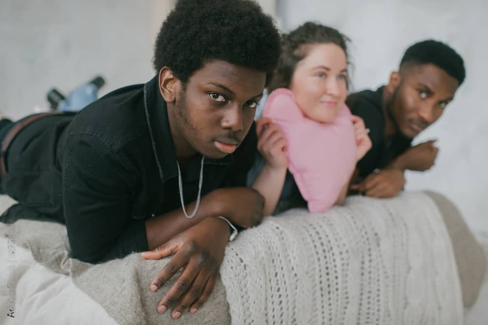 Um grupo de jovens deitados em uma cama, explorando o impacto social e cultural da pornografia inter-racial.